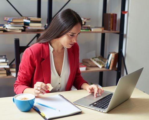 47778619 - young woman working with laptop and eating cookies in office